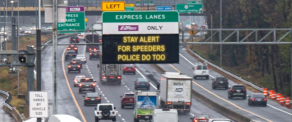 A road sign over a busy motorway with text warning motorists to 'stay alert for speeders'.