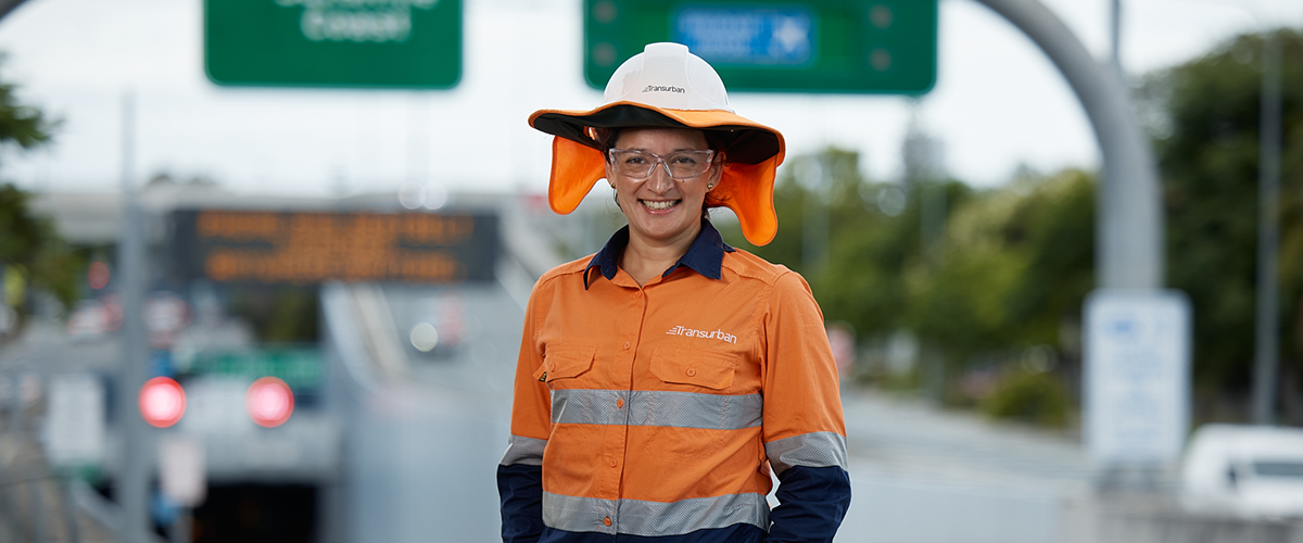 Woman stands in high-vis clothing in front of street signs